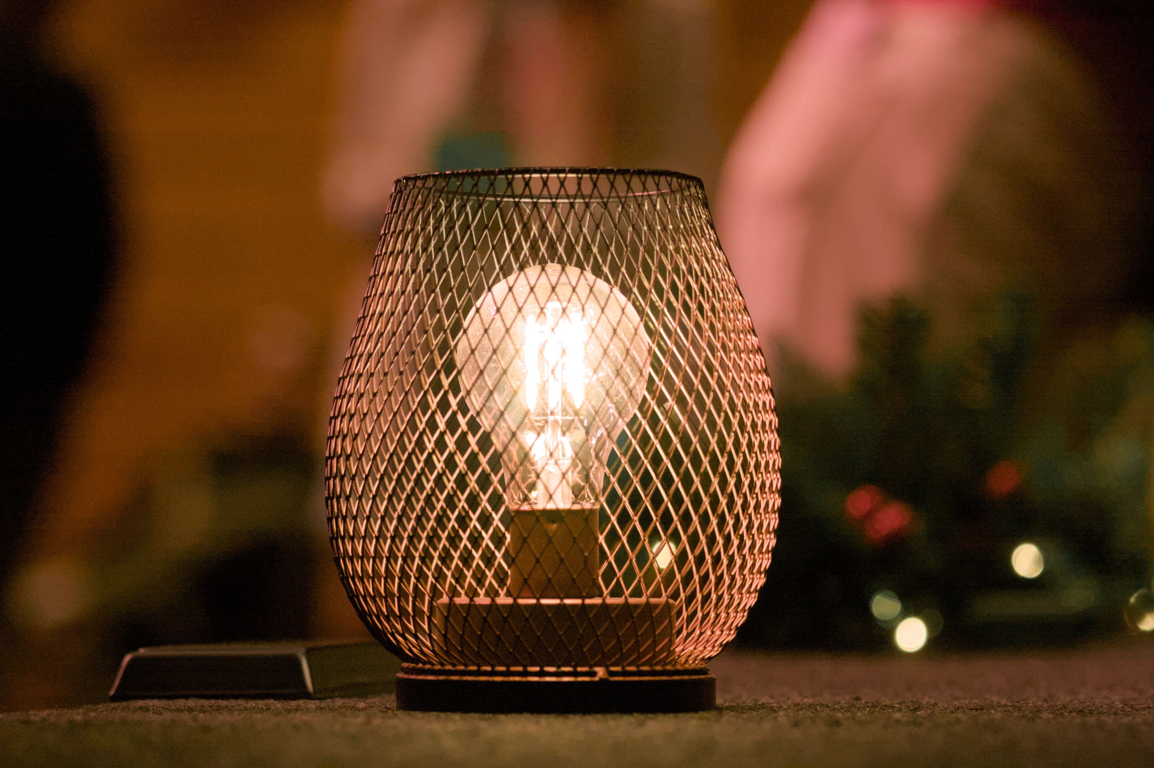 A glowing bulb enclosed by a black wire shade