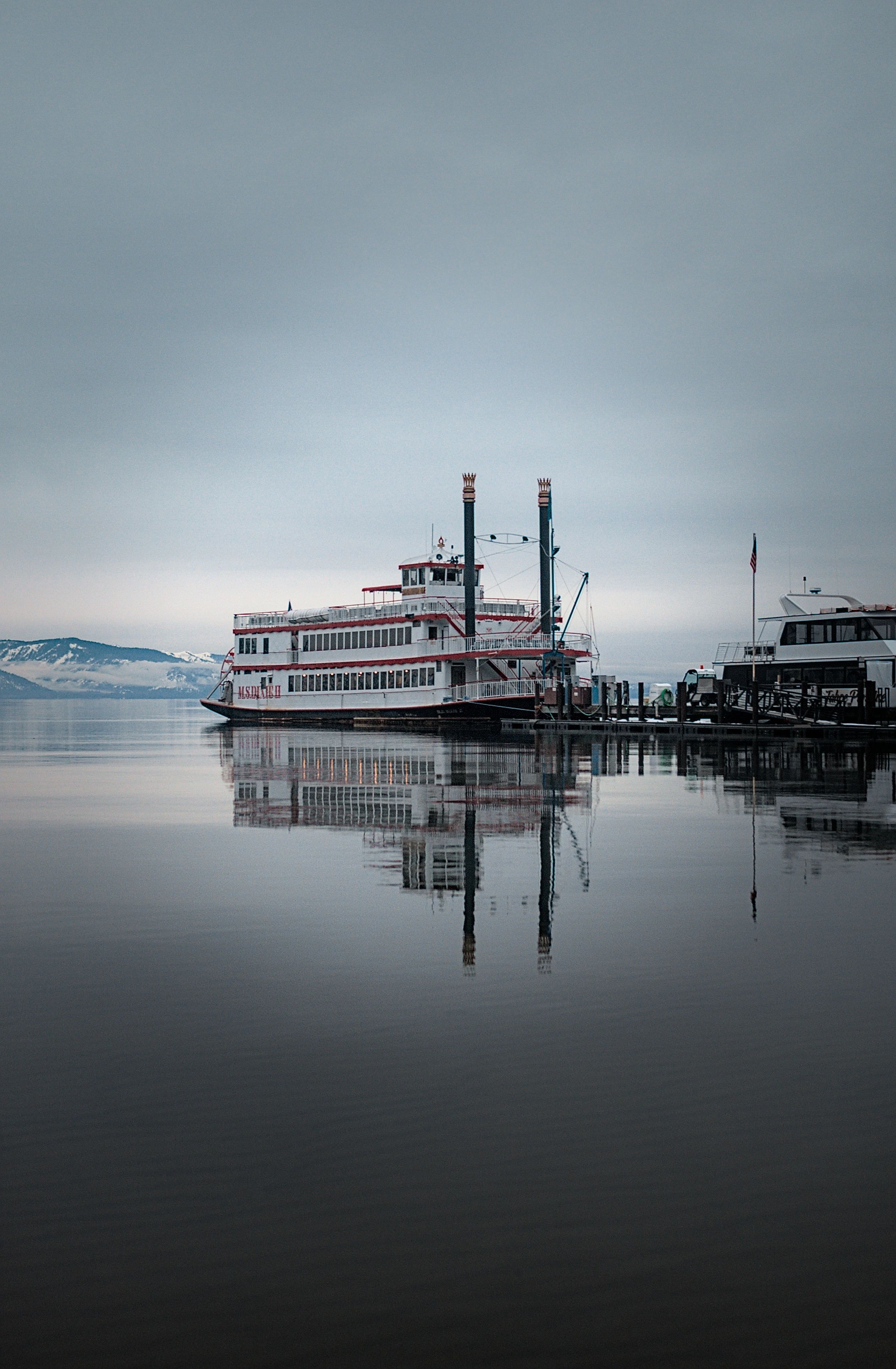 A paddlewheel boat and its reflection resting on the still gray water of Zephyr Cove